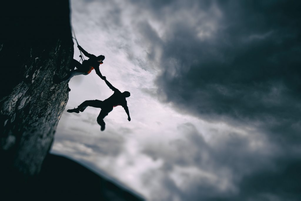 Rock climber helping the other up a cliff in a dramatic setting